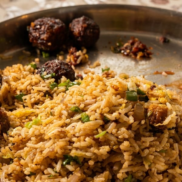 Close-up of fried rice with dark brown Manchurian balls on a metal plate.