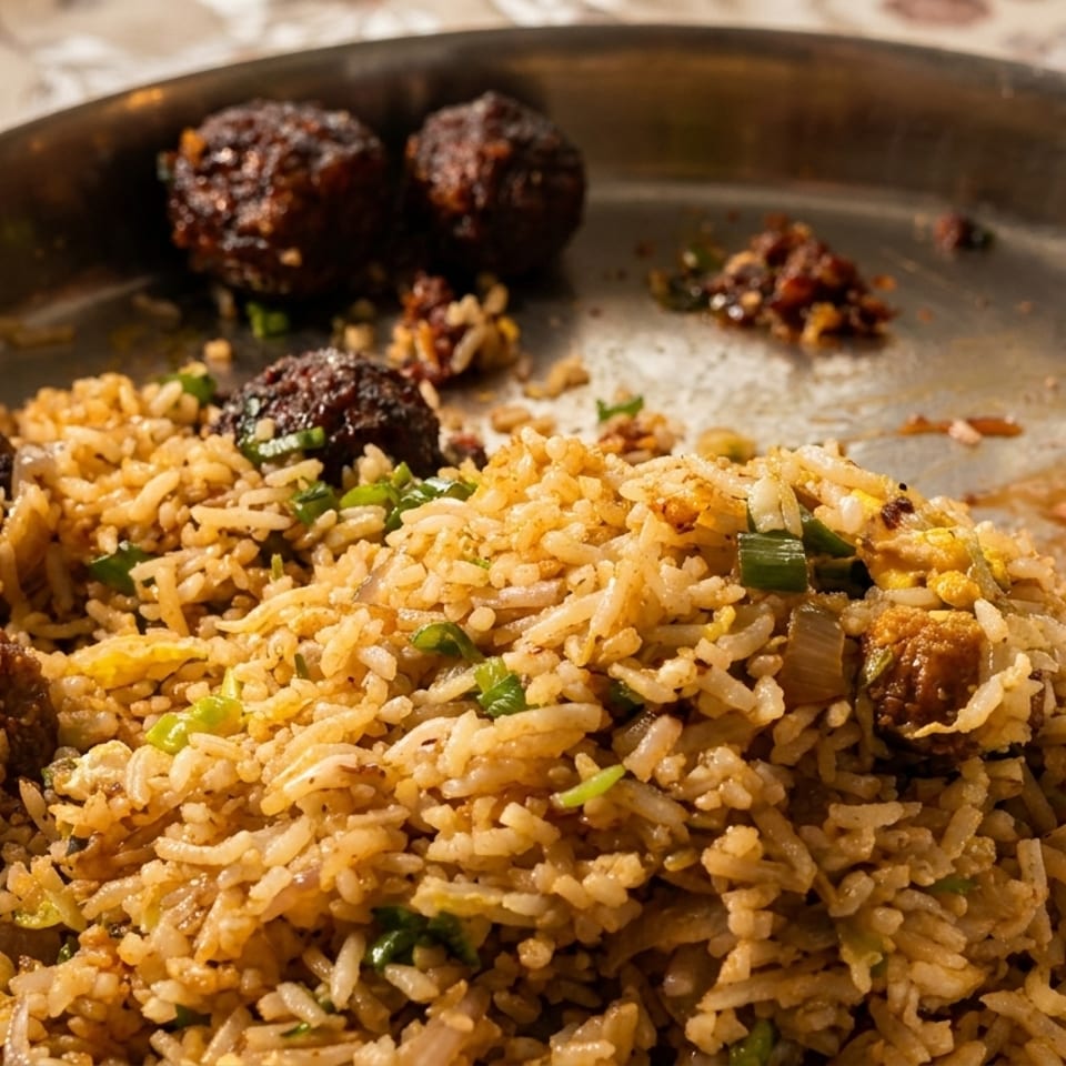 Close-up of fried rice with dark brown Manchurian balls on a metal plate.