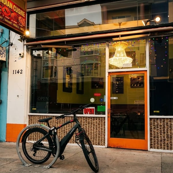 A bicycle parked outside an Indian cuisine restaurant with a bright orange door and chandelier.